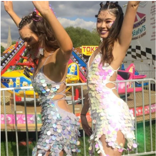 Two rave girls wearing sequin low cut backless dresses at a rave or music festival.