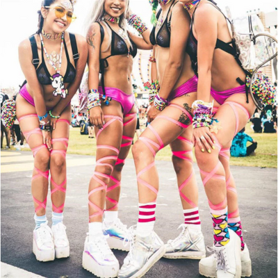 A group of raver girls wearing metallic leg wraps at electronic dance music festival.